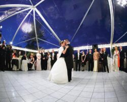 Wedding in a 40' x 60' tent featuring a clear top, chandeliers, and white dance floor.