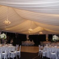 Medium silver chandeliers in a 40' x 80' frame tent with tent liner back lit with white lighting