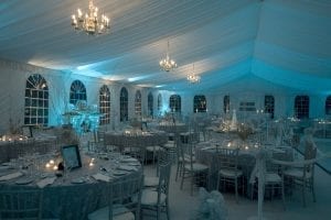 Black tie fundraiser held in a 50' x 90' frame tent featuring a tent liner back lit in blue, chandeliers, white carpet, and silver ballroom chairs.
