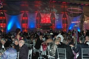 Black tie gala held in an airport hanger featuring color washed spandex panels, creative centerpieces, and silver ballroom chairs.